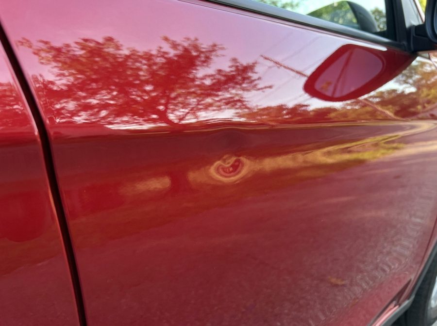 Door ding on a glossy red car door before repair