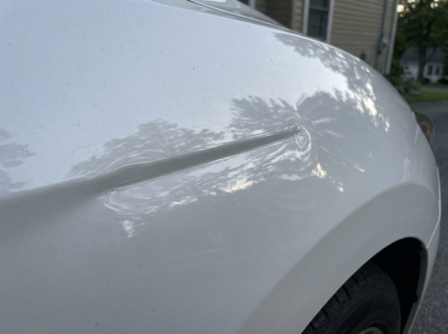 Crease dent on a white car fender before repair